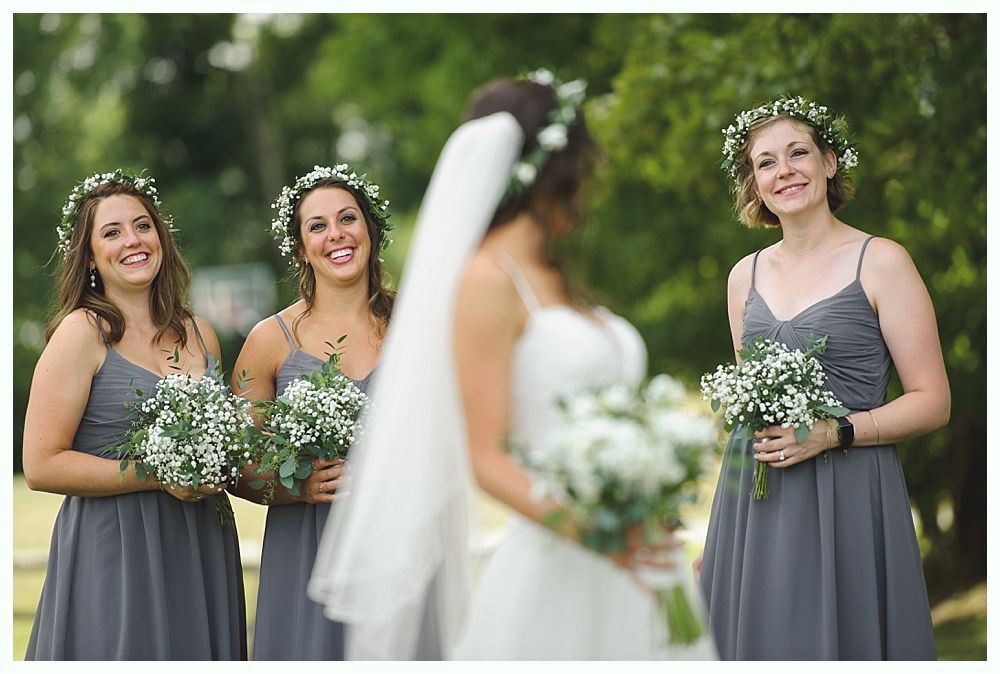 Bride with bridesmaids, all wearing flower crowns, holding bouquets, smiling outdoors.