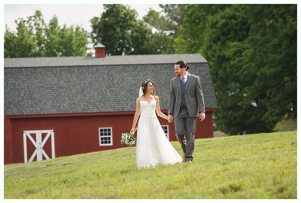 Groomsmen stand outside a red barn; they wear vests, bow ties, suspenders, and jackets draped over their shoulders.