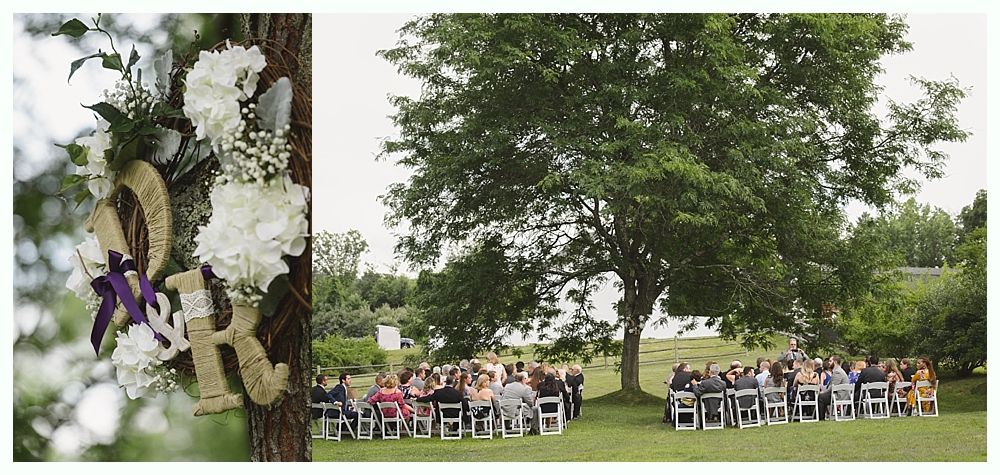 Wedding ceremony under a large tree; guests seated in white chairs. Initials and flowers on tree.