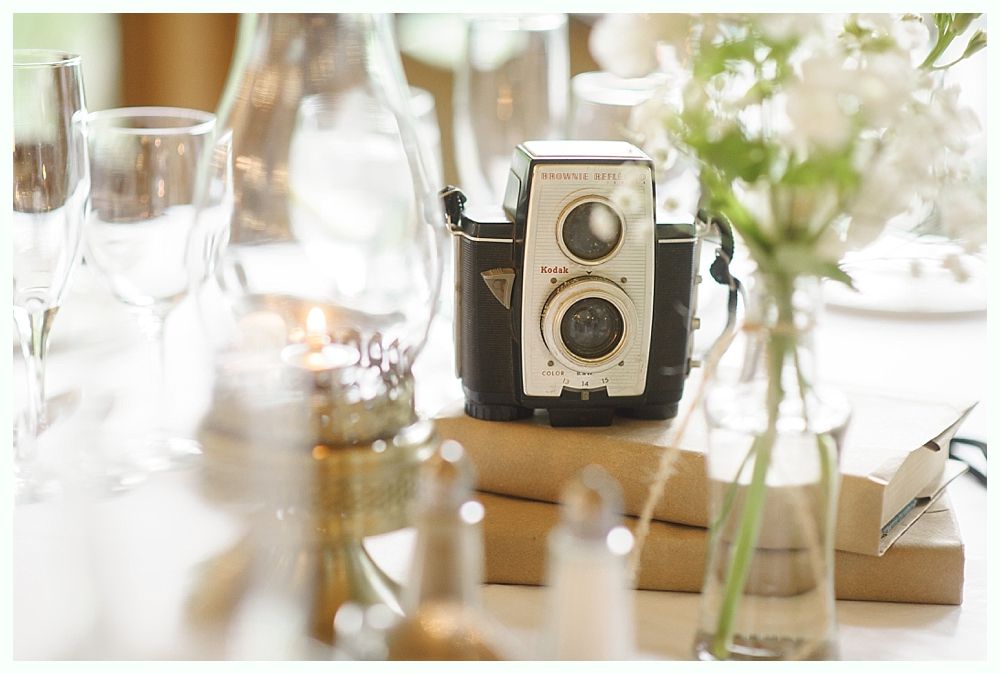 Vintage camera atop books on a table with flowers, candles, and glassware.