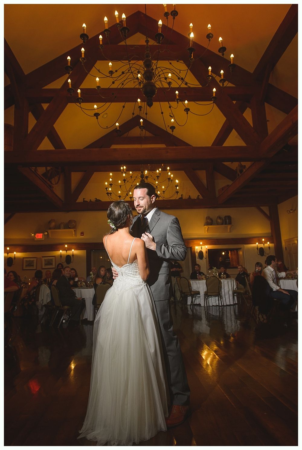 Couple dancing at a wedding reception, wooden ceiling, chandelier, soft lighting.