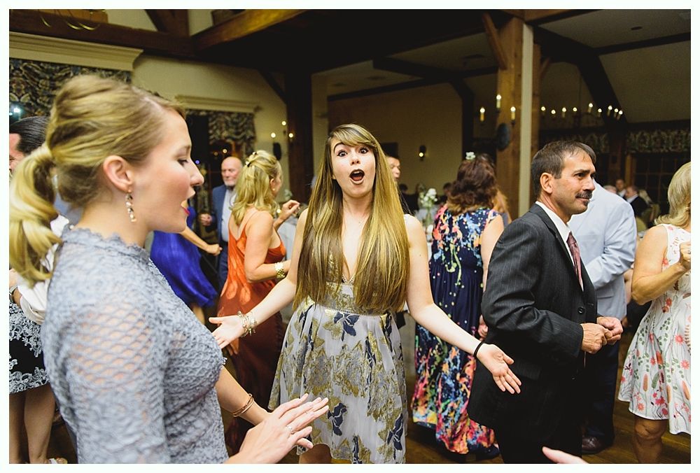 People dancing at a wedding reception. Woman with surprised expression, arms outstretched. Others in background.