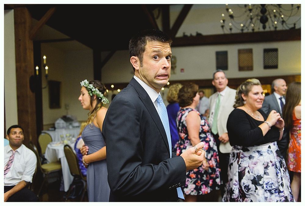 Man with surprised expression in formal attire at a wedding reception. People in background.