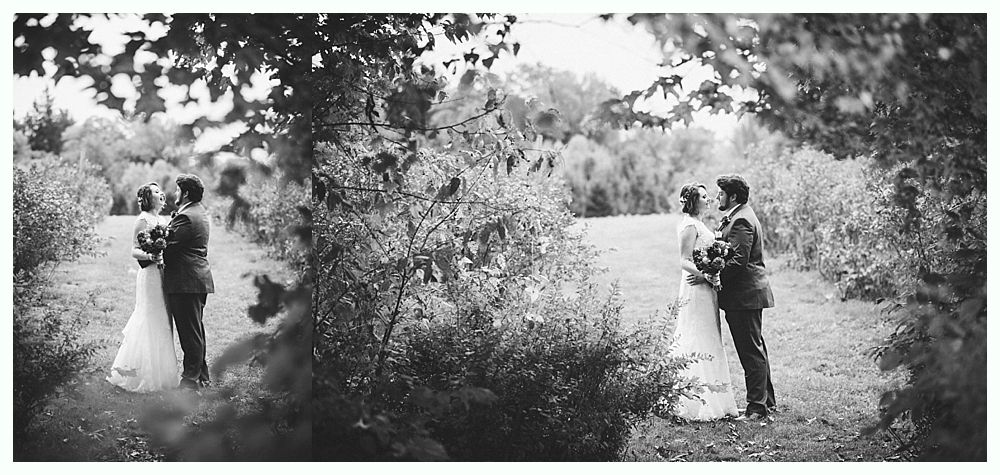 Newlyweds embrace in a wooded area, surrounded by foliage. Black and white photo.