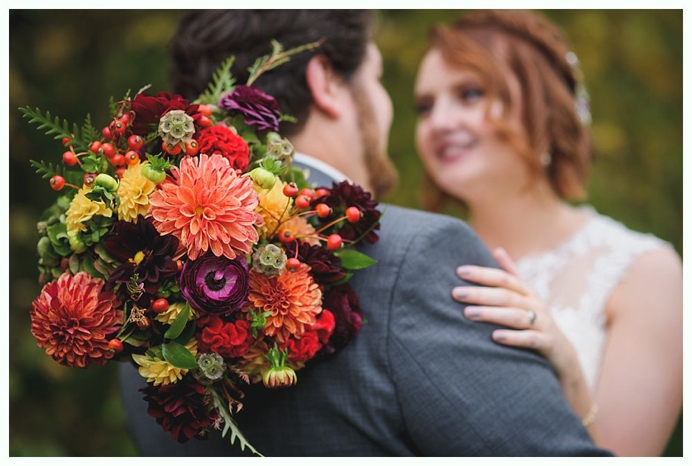 Bride and groom embrace, colorful bouquet in foreground.