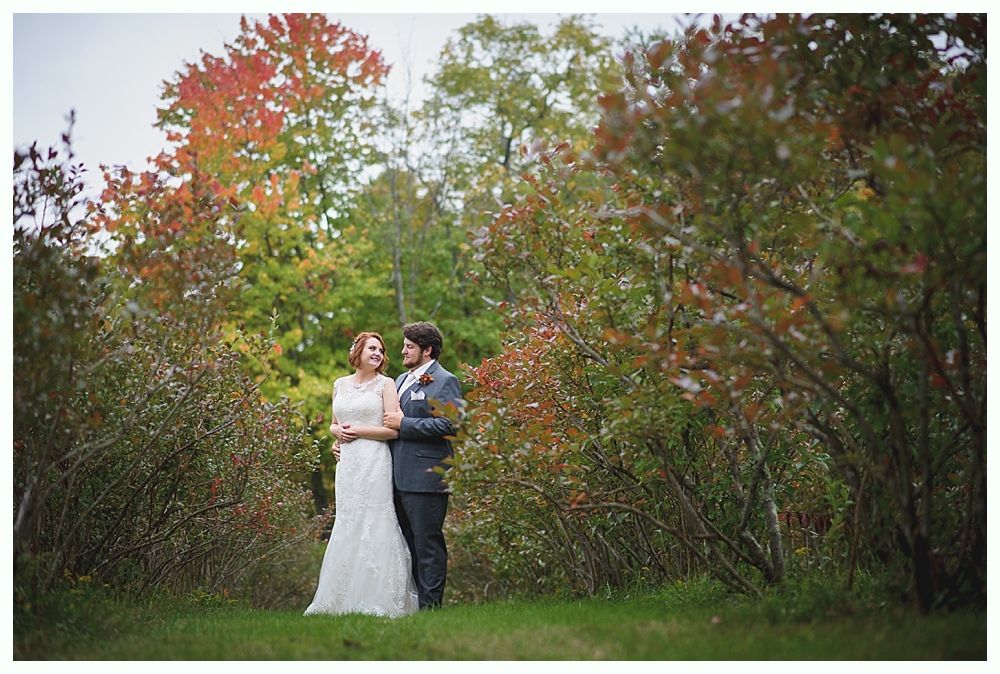 Bride and groom embracing in a field, autumn foliage overhead.