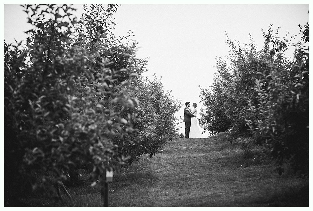Couple standing together on a hill, framed by trees in black and white.