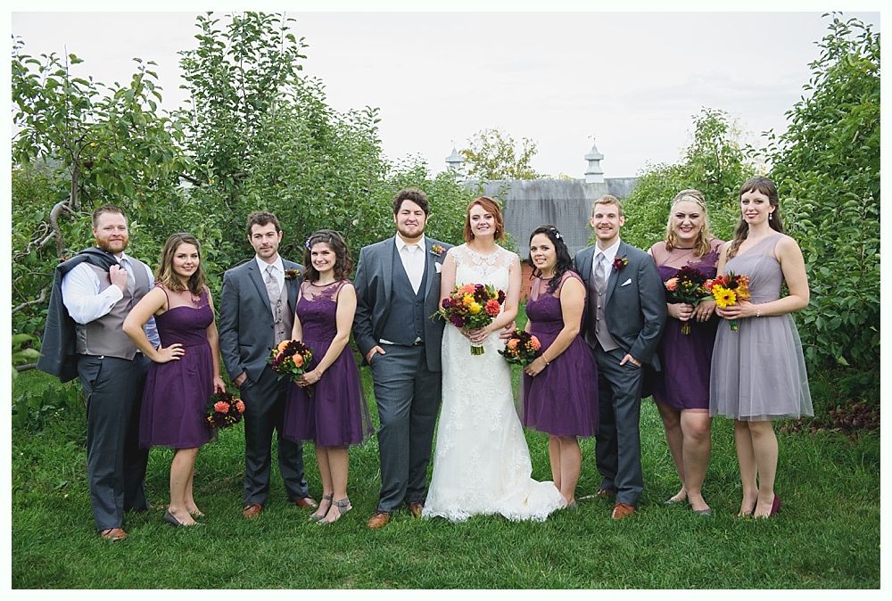 Wedding party: couple and attendants in formal attire, outdoor setting, greenery, holding bouquets.