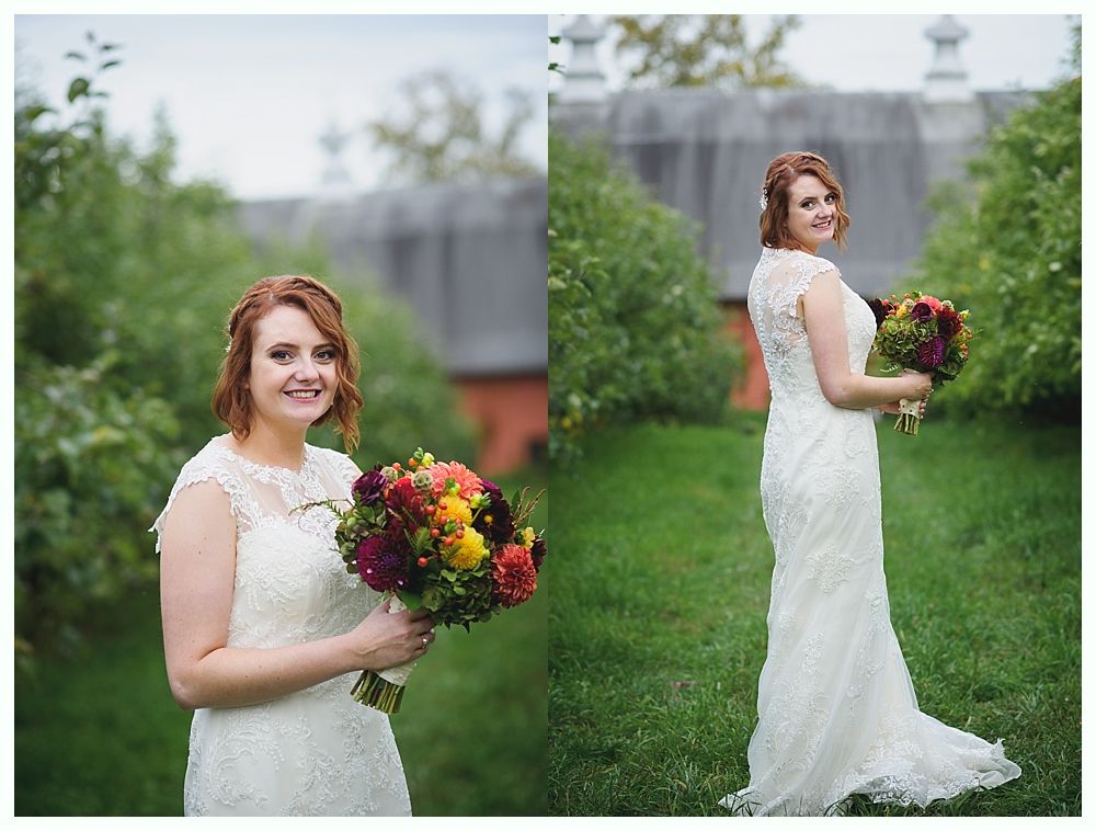 Bride in white lace dress holds colorful bouquet outdoors, smiling at the camera.