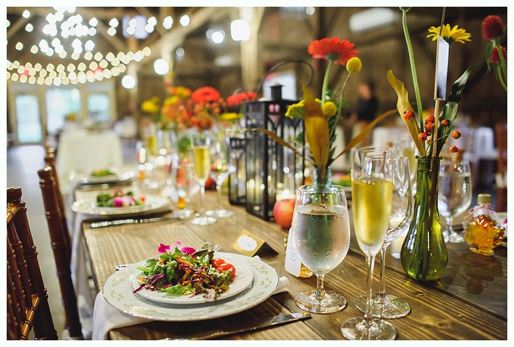 Long wooden table set for a celebration, decorated with flowers, candles, and glassware.