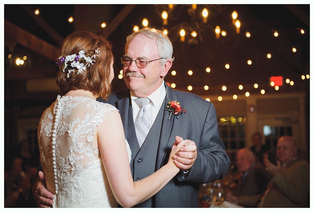 Father and bride share a dance at a wedding reception, under string lights.