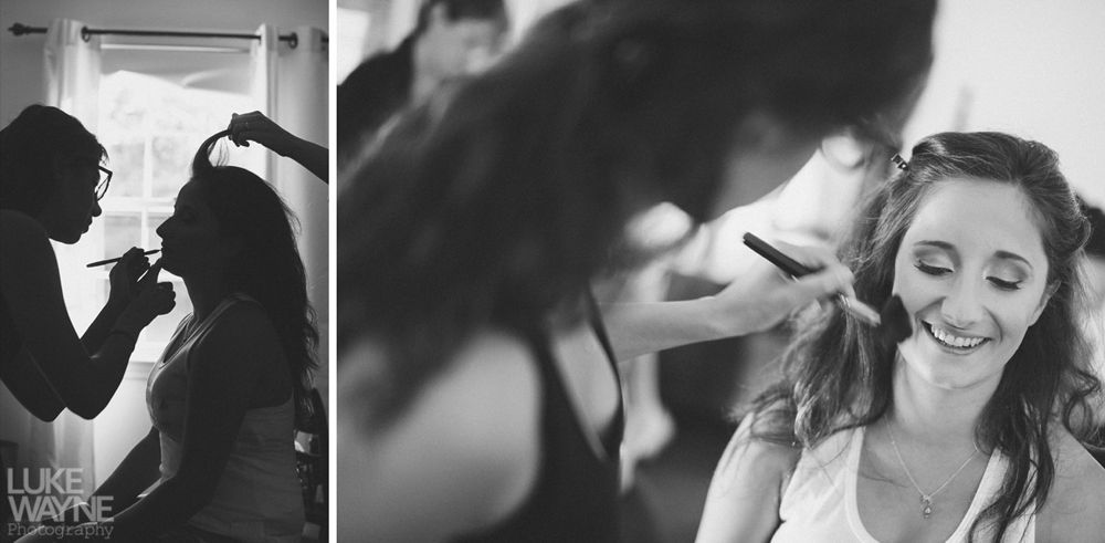 Makeup artist applying makeup to a smiling person. Another person in background assists with hair.