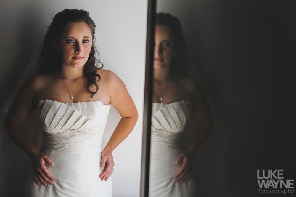 Bride in white strapless dress poses with hands on hips, next to a reflective dark surface.
