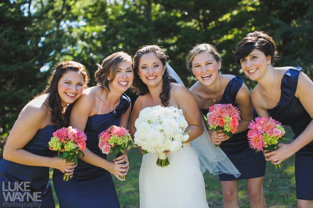 Bride and bridesmaids smiling with bouquets, wearing navy dresses, outdoors.