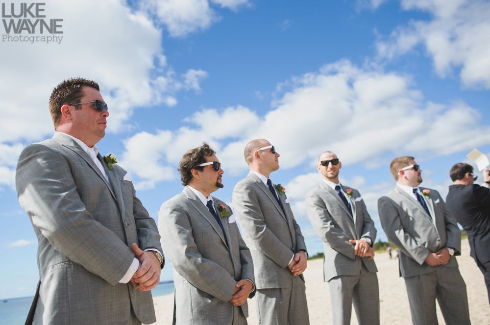 Men in gray suits and sunglasses stand outdoors, blue sky with clouds.