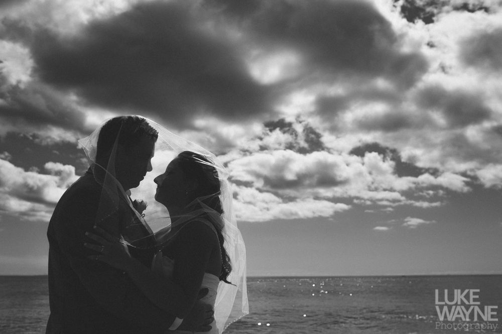 Silhouette of a couple facing each other, embracing, with a cloudy sky and ocean backdrop.