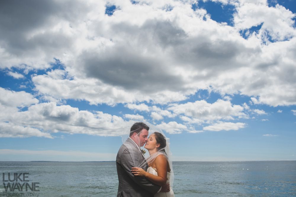 Couple kissing, silhouetted against ocean and sky with puffy clouds.