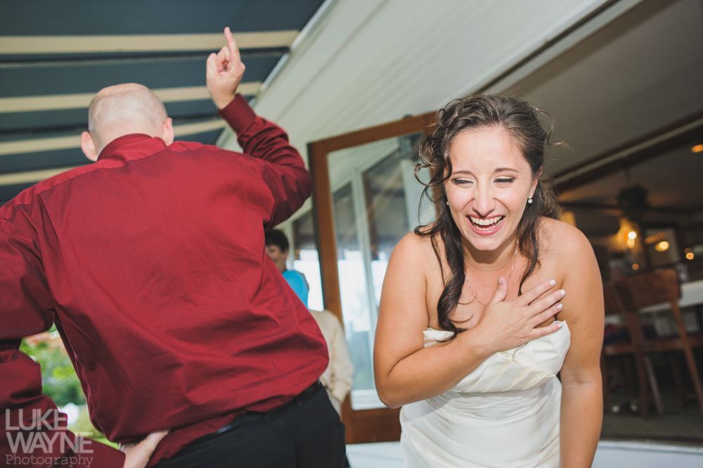 Bride laughs as man dances with raised finger at wedding reception.