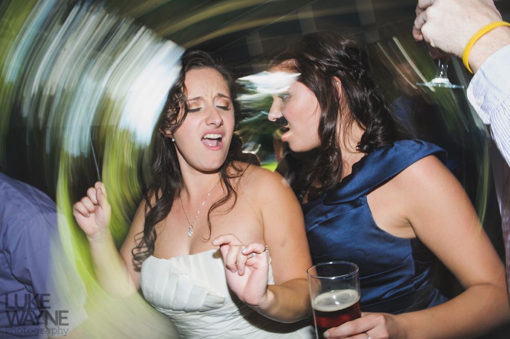 Two women dancing at a party; one in a white dress, the other in blue, with a beer in her hand.