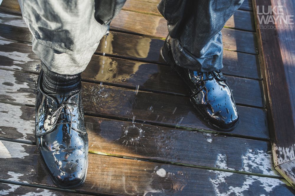 Person's wet, black shiny shoes and jeans on a wooden dock; light reflections.
