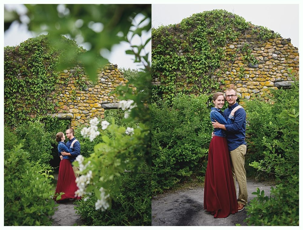Couple hugging in a garden, with ivy-covered stone wall background. Woman in red skirt, man in blue shirt, embracing.