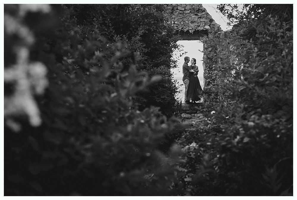 Couple embraces in doorway, surrounded by foliage. Black and white.