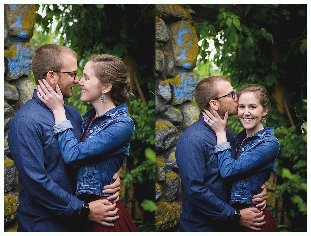 Couple embraces outdoors; man kisses woman's cheek. Wearing denim jackets, holding hands near a stone wall.
