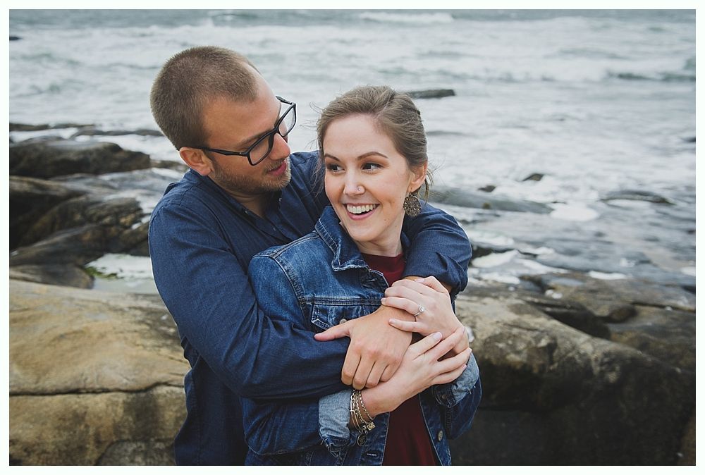 Man hugging woman from behind, smiling by the ocean.