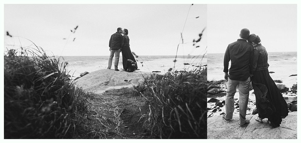 Couple standing on a rocky shore, looking out at the water. Black and white.