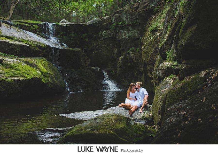 Couple sitting on a rock near a waterfall in a lush, green forest.