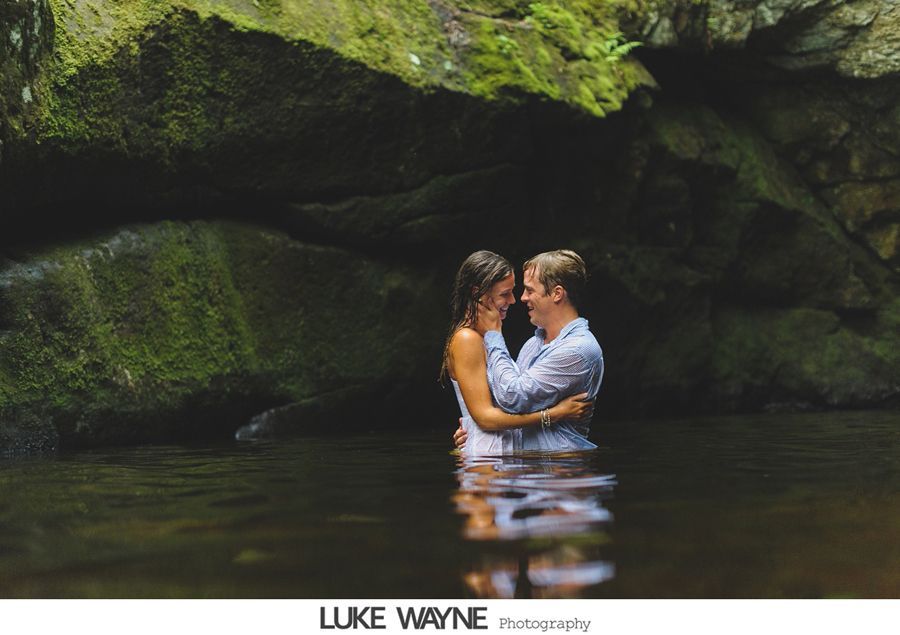 Couple embraces in a stream, laughing. They are surrounded by mossy rocks.