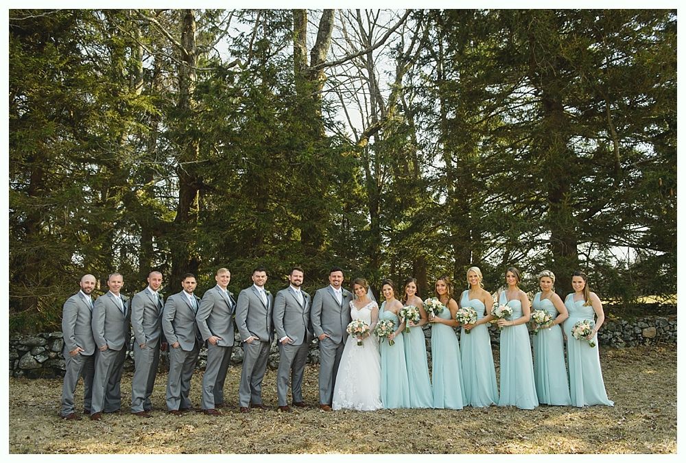 Wedding party of groomsmen in gray suits and bridesmaids in teal dresses, outdoors.