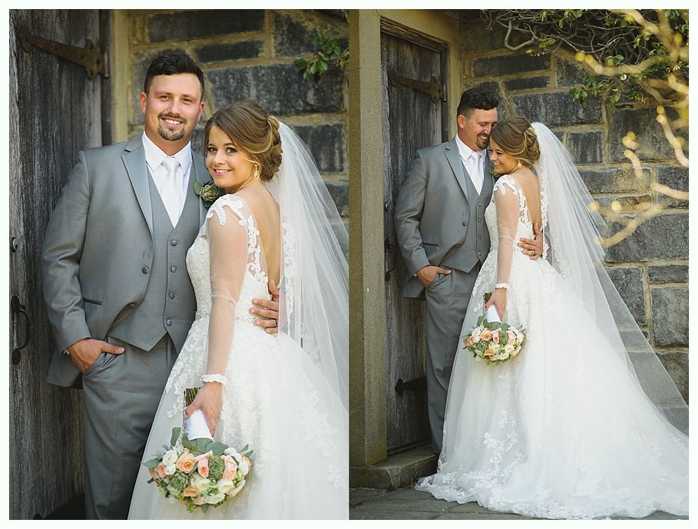Bride and groom posing for photos outside stone building. Bride in white gown with veil, holding bouquet. Groom in gray suit.