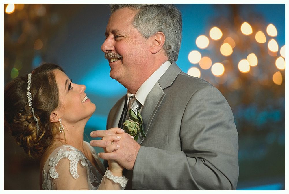 Bride and groom smiling while dancing at wedding reception, background with bokeh lights.