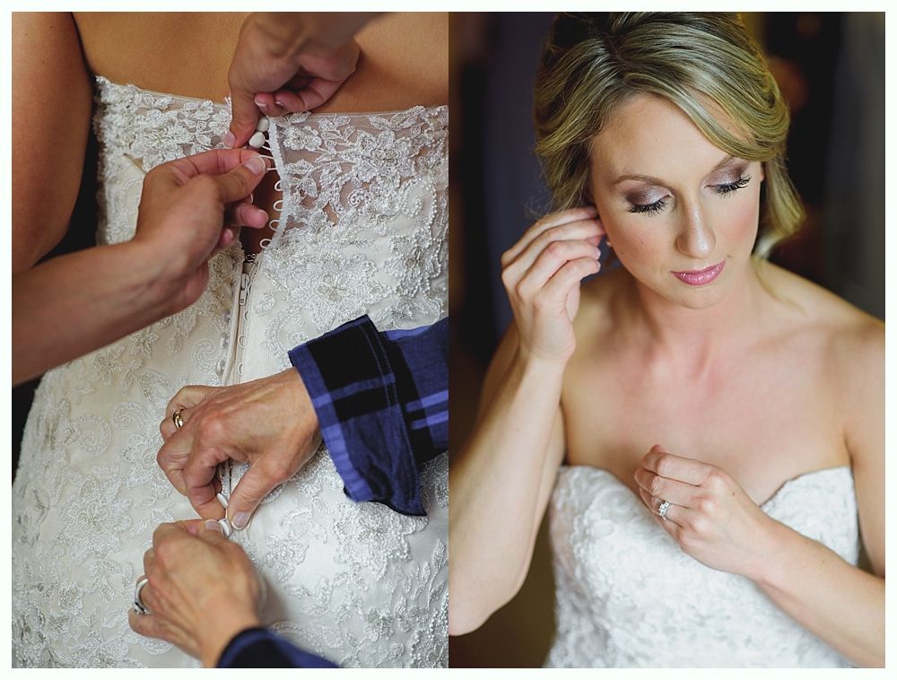 Bride in wedding dress, tattoos visible, putting on earrings, holding bouquet with ring.