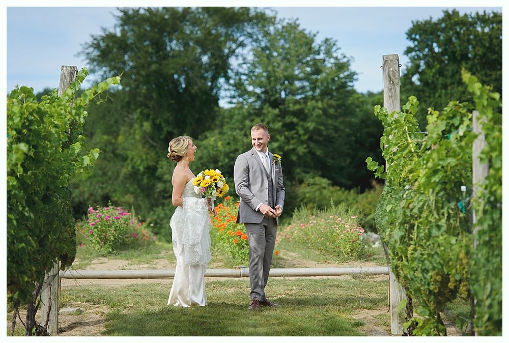 Bride and groom smiling at camera, bride holds bouquet, man in blue suit. Outdoor setting.