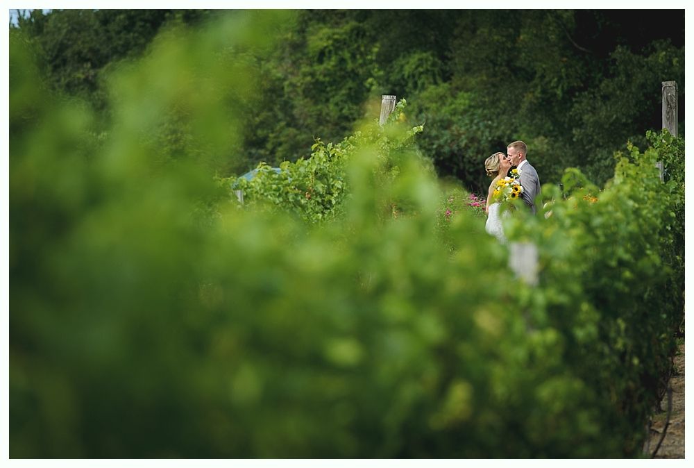 Newlyweds pose in front of a weathered barn. The bride wears a white gown and veil, while the groom wears a navy suit.