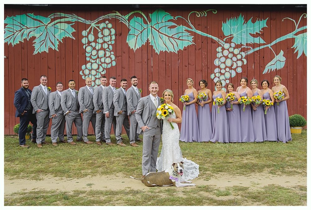 Bride in a wedding dress kisses a baby wearing a matching dress and flower headband. Outdoors with greenery.