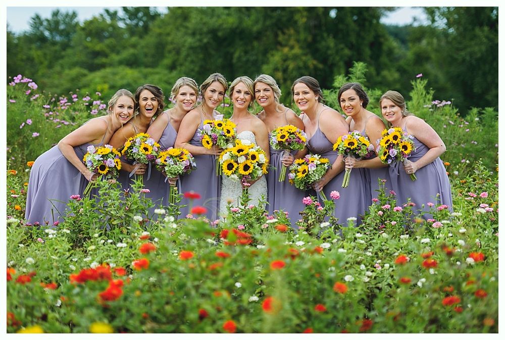 Bride with bridesmaids in gold gowns holding bouquets outdoors.