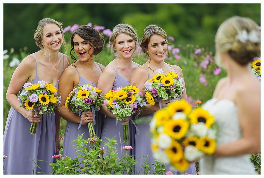 Four women in gold sequined gowns hold bouquets, smiling in a field.