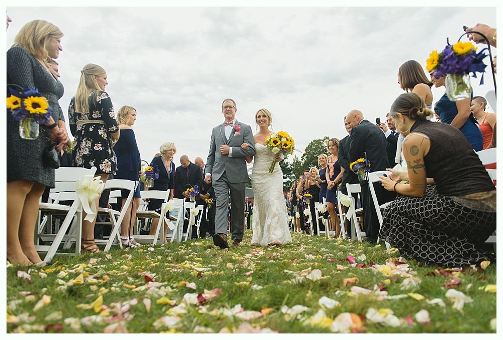 Groom smiling at bride during wedding ceremony; groomsmen in navy suits stand beside him.