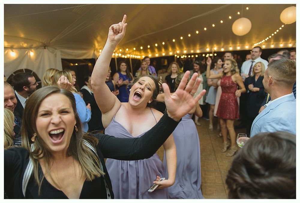 Four women in gold sequin dresses, laughing and hugging, at a party with blue lighting.