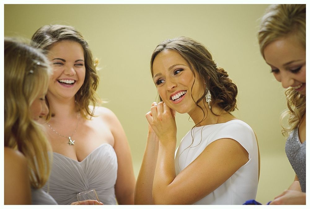 Bride and groom on rocky shoreline, ocean and blue sky background. Groom in suit, bride in white dress, looking at each other.
