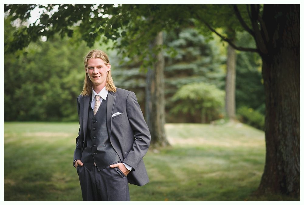 Bride with arms up, making a funny face, groom looking at his hand, cake cutting in background.