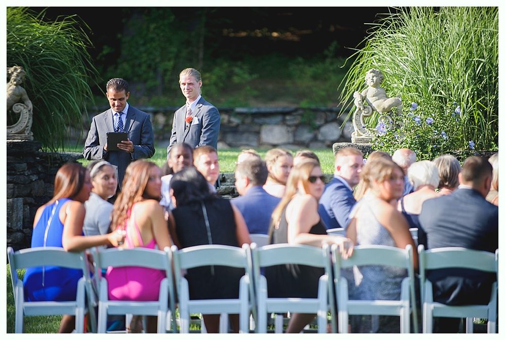 Bride with arms up, making a funny face, groom looking at his hand, cake cutting in background.