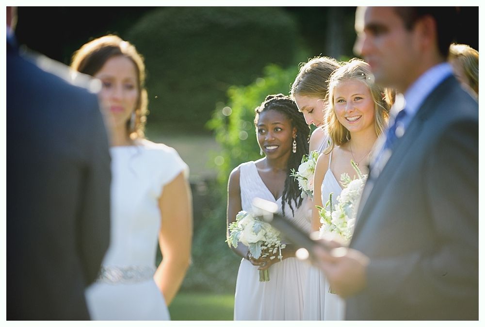 Bride with arms up, making a funny face, groom looking at his hand, cake cutting in background.