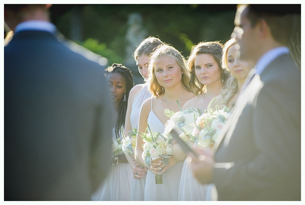 Bride with arms up, making a funny face, groom looking at his hand, cake cutting in background.