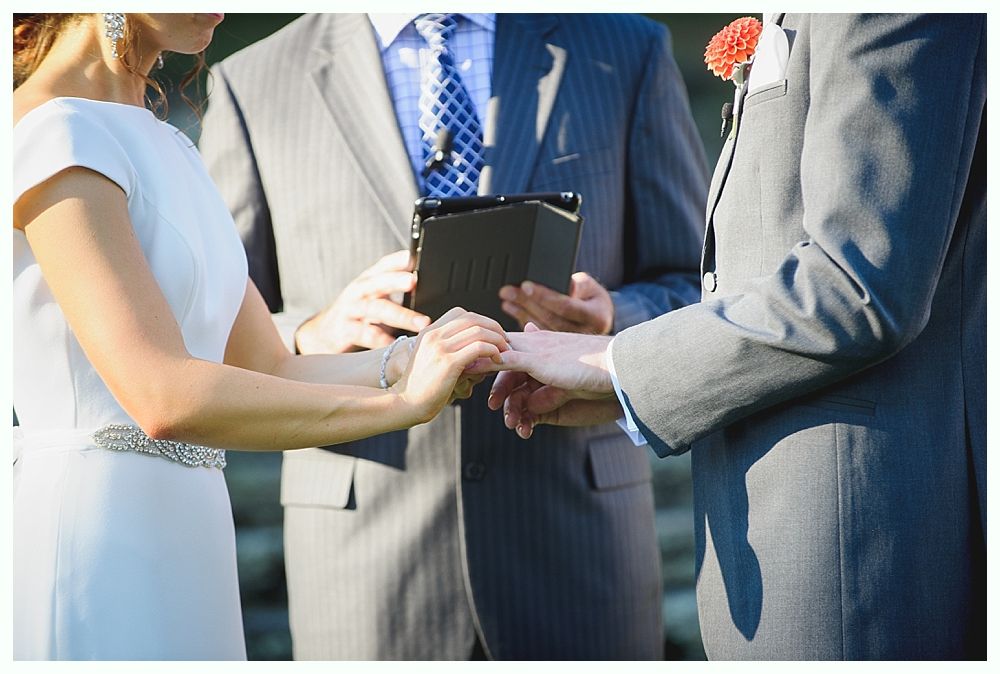Bride with arms up, making a funny face, groom looking at his hand, cake cutting in background.