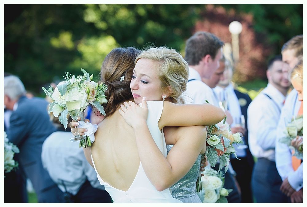 Bride with arms up, making a funny face, groom looking at his hand, cake cutting in background.