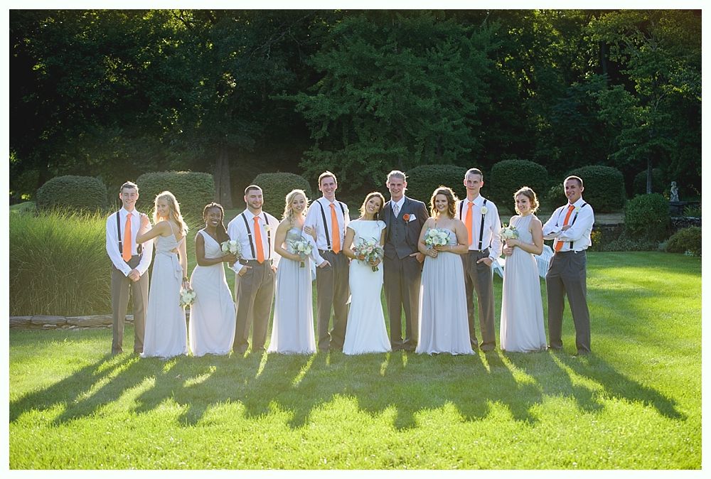 Bride with arms up, making a funny face, groom looking at his hand, cake cutting in background.